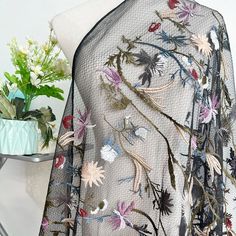 an embroidered shawl on a mannequin next to a vase with flowers in it