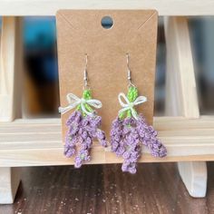 purple crocheted flower earrings with green ribbon on wooden table next to cardboard package