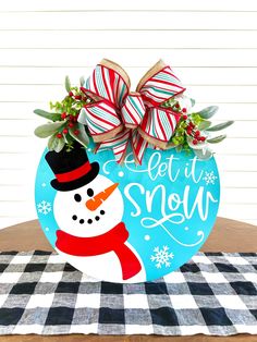 a wooden sign with a snowman on it that says let it snow in front of a checkered tablecloth