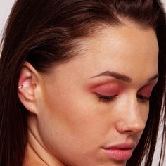 a woman with pink eyeshadow and piercings on her left ear looking down