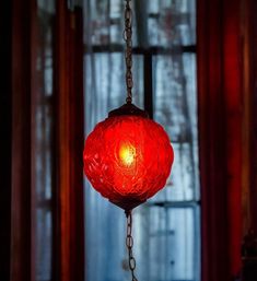 a red light hanging from a chain in front of a window