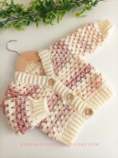 a crocheted sweater with buttons and a wooden hanger next to some green leaves