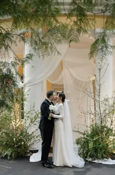 a bride and groom standing in front of a building with white drapes on it