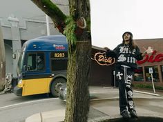 a man standing next to a tree in front of a blue and yellow bus on the street