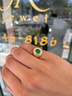 a person's hand holding a ring with a green stone in the middle and gold on it