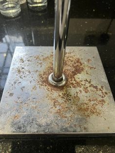 a metal object with rust on it sitting on top of a black table next to glasses