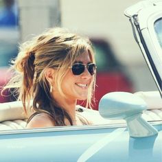 a woman sitting in the driver's seat of a blue car with her hair pulled back