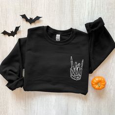 Halloween Shirt, Skeleton Rock Shirt, Halloween Skeleton T-Shirt, Skeleton Hand Halloween, Halloween Gift, Horror Shirt Sweatshirt Description Our graphic sweatshirts are very soft, very cute and bound to keep you warm in the colder months. It's a pre-shrunk, classic fit sweater made with air-jet spun yarn for a soft feel. ► SHIRT DETAILS The sweatshirts are UNISEX - they are meant to have a relaxed fit, please refer to the size chart for more details. * 8.0 oz., 50/50 cotton/polyester * Pre-shr Halloween Skull Print Sweatshirt For Streetwear, Black Grunge Sweatshirt For Fall, Grunge Halloween Sweater For Streetwear, Halloween Sweatshirt For Streetwear, Spooky Black T-shirt For Winter, Halloween Grunge Long Sleeve Sweater, Black Cotton Sweatshirt With Skull Print, Spooky Long Sleeve T-shirt For Winter, Spooky Long Sleeve Black Sweater