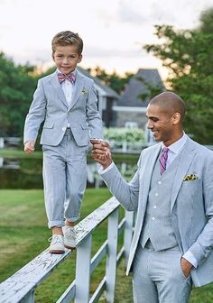 a man in a suit and tie holds the hand of a young boy who is standing on a rail