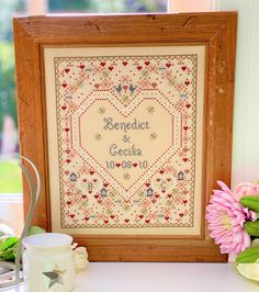 a cross - stitch heart is displayed in front of a window with flowers and candles