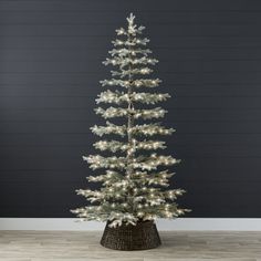 a white christmas tree in a basket with lights on the top and bottom, against a black wall