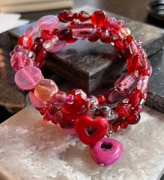 Heart bracelet. Red and pink glass beads on silver memory wire. At each end of the bracelet is a metal heart and a stone heart. Adjusts to your wrist size. Valentine's Day Beaded Bracelets With Heart Charm, Valentine's Day Heart Beaded Bracelets, Valentine's Day Heart Beads Stretch Bracelet, Valentine's Day Heart-shaped Beaded Bracelets, Pink Heart-shaped Spiritual Beaded Bracelets, Valentine's Day Hand-strung Round Bead Jewelry, Valentine's Day Heart-shaped Stretch Bracelet With Heart Beads, Valentine's Day Heart-shaped Colorful Beaded Bracelet, Red Heart Beads Bracelet For Valentine's Day