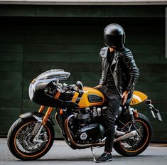 a man in black leather jacket standing next to an orange and black motorbike