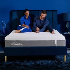 a man and woman sitting on top of a tempur - pedic mattress