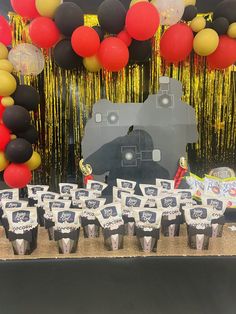 a table topped with lots of cupcakes next to a wall covered in balloons