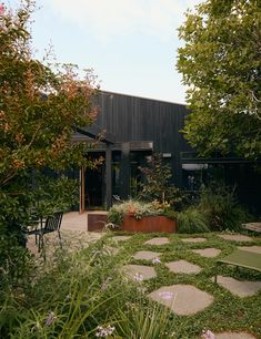 a black building surrounded by lush green trees and plants with stepping stones in the foreground