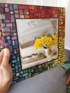 a person holding up a colorful mirror with yellow flowers in the reflection and a woman's hand touching it