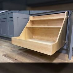 an empty wooden shelf in the middle of a kitchen with gray cabinets and wood flooring