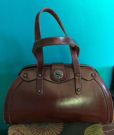 I am offering this graceful yet sturdy bag from the late 1950s/early 1960s. This dark brown leather bag has a nice hard satchel design with a nice mezzanine Luna curve. It has a double top handle and a pretty little keyhole latch. Please, be aware that their a little wear and mini mail scratches. Mid-century Brown Shoulder Bag For Travel, Vintage Formal Bags With Leather Lining, Vintage Formal Bag With Leather Lining, Vintage Brown Shoulder Bag For Office, Vintage Leather Evening Satchel, Vintage Leather Satchel For Evening, Vintage Brown Retro Satchel For Daily Use, Retro Vintage Brown Satchel For Daily Use, Mid-century Brown Satchel Bag