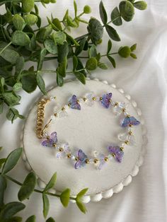 a bracelet with purple and white butterflies on it sitting next to some green leaves in the background