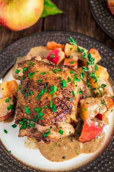 a plate topped with meat covered in gravy next to potatoes and apples on a wooden table