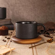 a black coffee cup sitting on top of a wooden coaster next to a muffin