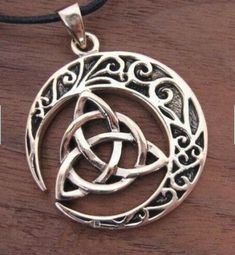 a silver pendant with an intertwined design on a leather cord necklace, sitting on top of a wooden table