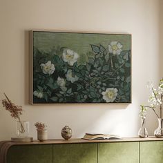 a painting hanging on the wall above a green cabinet with vases and flowers in it