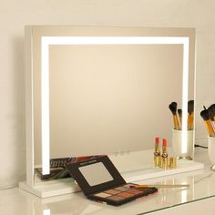 a vanity mirror with lights and makeup brushes on top of it next to a vase