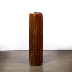 a tall wooden vase sitting on top of a hard wood floor next to a white wall