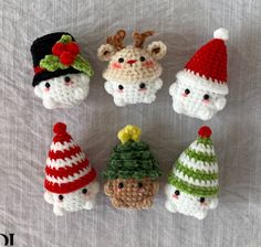 six crocheted christmas ornaments are arranged on a white sheet, one is wearing a santa claus hat and the other has a reindeer's head