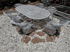 an outdoor table and chairs on gravel area next to metal wire baskets with plants in them