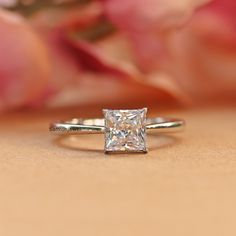 a close up view of a ring with a princess cut diamond in the center on a table