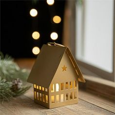 a house shaped candle holder on a wooden table with christmas lights in the back ground