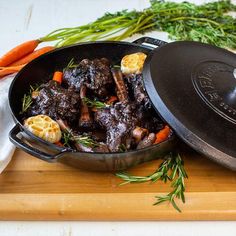 a pot filled with meat and vegetables on top of a wooden cutting board next to carrots