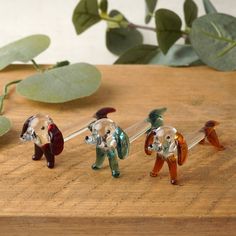 four glass figurines of different animals on a wooden table next to green leaves