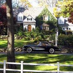 an old black car parked in front of a large house on the side of a road