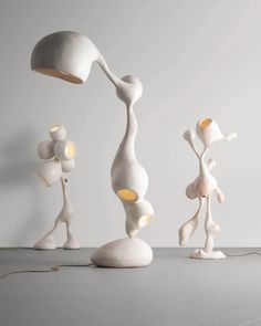 three white sculptures with one light on and the other standing up in front of it