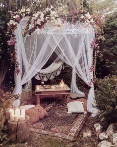 a canopy bed with white curtains and flowers on it is surrounded by greenery in the woods