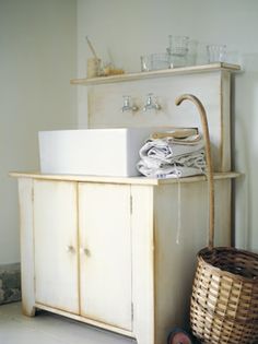 a white sink sitting next to a wooden cabinet and wicker basket on the floor