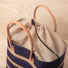 Looking for a unique and gorgeous beach tote? This raffia bag is made from high-quality raffia palm with a natural and navy blue alternating stripe. These bags have a useful cotton pull closure, inside pocket, and beautiful zebu leather handles, and are big enough to handle even the longest beach days! All our raffia totes are made by a fair-trade woman-owned company in Madagascar. 100% raffia eco-friendly dyes zebu leather handle inside pocket cotton pull closure 17.5" x 13.5" x 8" 7" handle dr Travel Striped Straw Bag With Braided Handles, Blue Travel Bag With Bamboo Handle, Navy Tote Beach Bag For Travel, Travel Beach Bag With Striped Lining, Navy Travel Bag With Braided Handles, Eco-friendly Handmade Top Handle Beach Bag, Blue Jute Travel Bag, Eco-friendly Beach Bag With Top Handle In Natural Color, Handwoven Striped Beach Bags