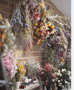 a room filled with lots of different types of flowers hanging from the ceiling next to a brick wall