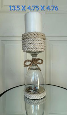 a glass table topped with a white candle and rope wrapped around the top of it