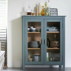 a blue cabinet with glass doors and dishes on it's shelves next to a white couch