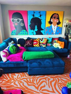 a living room filled with blue couches covered in pillows and colorful paintings on the wall