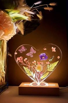 a glass heart with flowers and butterflies on it sitting next to a vase filled with flowers