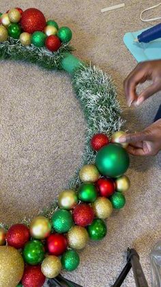 someone is making a christmas wreath out of balls and tinsel on the floor with scissors