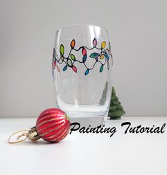 a glass with christmas lights painted on it next to a red ornament and small tree