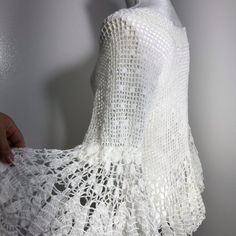 a white crochet dress is being held up by a person's hand