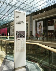 a white sign sitting in the middle of a mall next to a glass wall with an advertisement on it